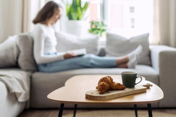 iStock Credit: brizmaker A wood living room table with a woman reading in the background